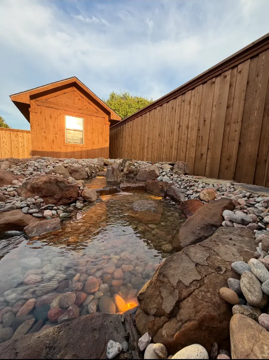 Completed backyard stream cascading over natural stone and river rock